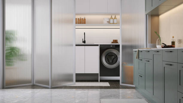 istock Modern design white frame, reeded glass panel folding door, partition between laundry room with washing machine, dryer, cabinet, cupboard and kitchen with sage green counter 1460971154
