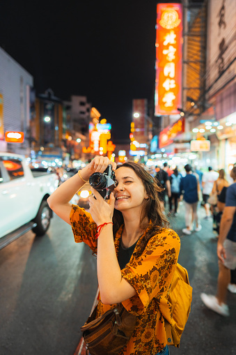 Cheerful young Caucasian woman photographing with camera in Chinatown, Bangkok