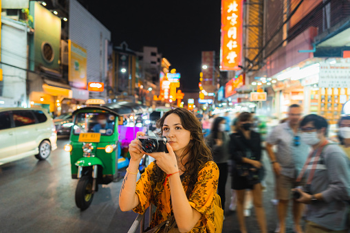 Cheerful young Caucasian woman photographing with camera in Chinatown, Bangkok