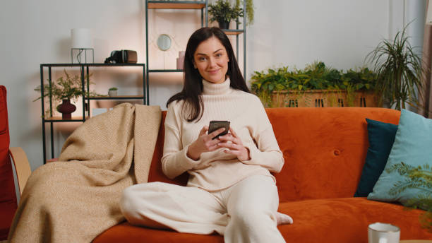 istock Young brunette woman sitting on sofa, using smartphone share messages on social media application 1460980575
