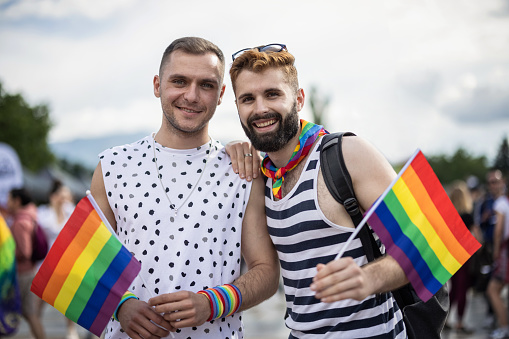 Two gay man waving pride flags and looking at camera