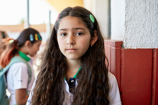 Head and shoulders view of longhaired 10 year old wearing private school uniform and looking at camera, classmate in background.