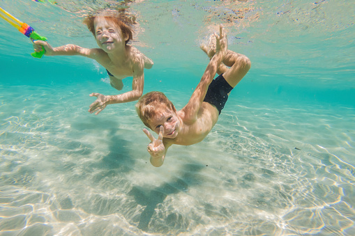 Cute boys swimming underwater in shallow turquoise water at tropical beach.