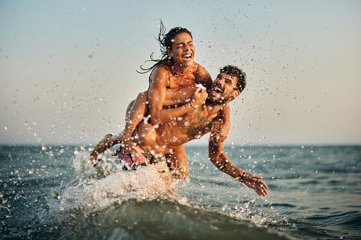 Cheerful couple having fun while piggybacking in summer day at sea. Copy space.