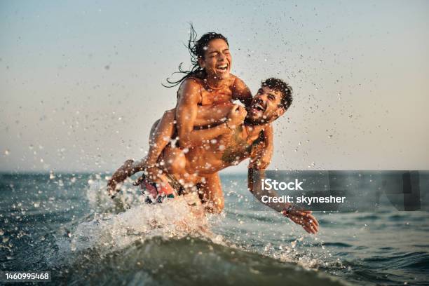 Young Playful Couple Having Fun While Piggybacking At Sea Stock Photo - Download Image Now