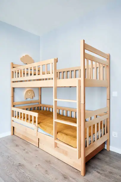 Wooden bunk bed and elegant minimalist interior design in apartment after renovation. Child bedroom with comfortable kid bed, laminate floor, white walls.