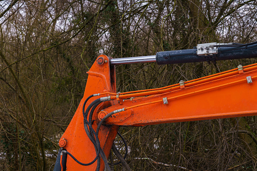 The hydraulic part of the excavator boom against the background of tree branches. Close up.