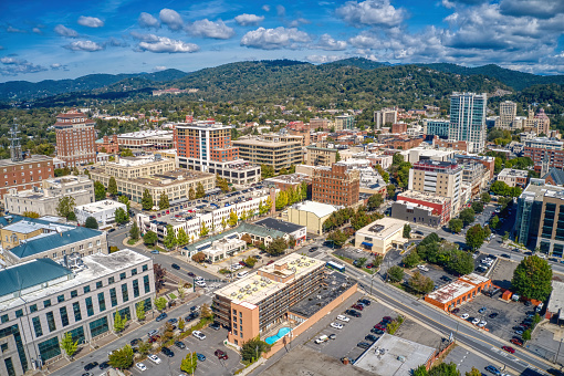 An aerial view of Asheville with dense buildings under a blue sky with fluffy clouds in North Carolina