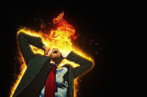 A desperate-looking businessman is surrounded by fire and flames as he holds his head and screams.