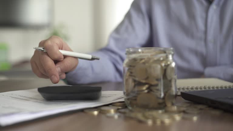 Close-up Adult man using calculator at home. coin jar on the table