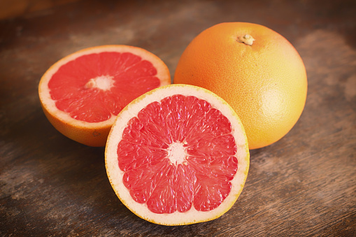 A closeup shot of a whole and a half-sliced grapefruit on a wooden surface