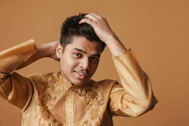 Young brunette indian man smiling and looking at camera isolated over yellow background