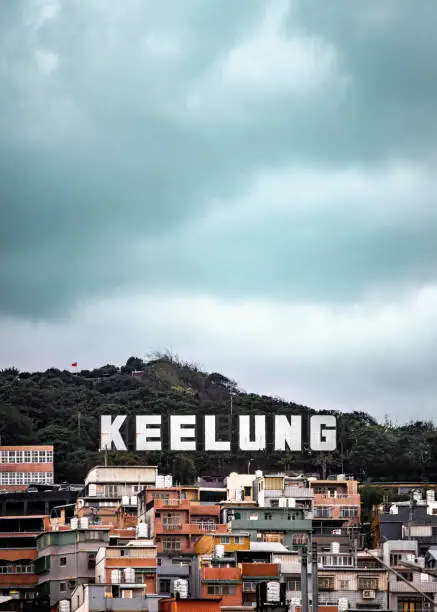 A vertical shot of a large Keelung sign above old houses on a hill in Taiwan