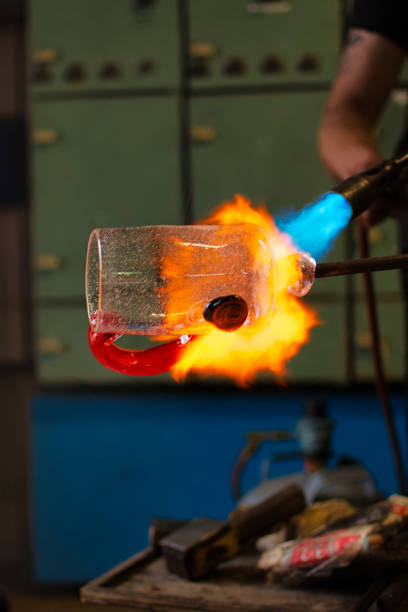 Vertical shot of a glassblower melting a glass in the workshop with a blurry background A vertical shot of a glassblower melting a glass in the workshop with a blurry background hand blown glass stock pictures, royalty-free photos & images