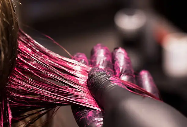 Photo of close-up coloring a strand of blond hair in a bright pink color, beauty salon