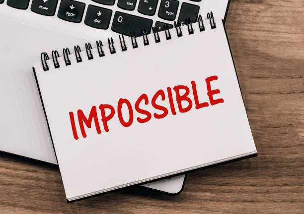 istock A notebook with the text IMPOSSIBLE lies on a laptop standing on a wooden table. 1461011916
