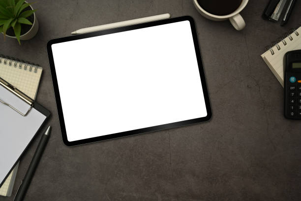 istock Flat lay digital tablet with white blank screen, cup of coffee and notepad on black slate texture background. 1461014758
