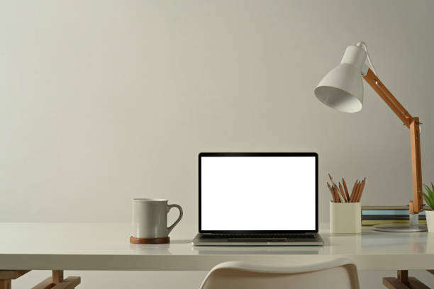 istock Front view of laptop computer, coffee cup, pencil holder and lamp on white table in minimal home office. 1461014863