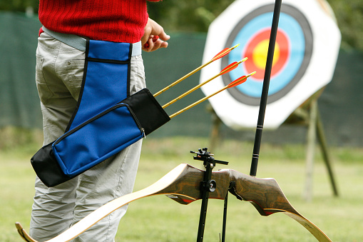 A closeup of a man shooting a longbow on the target in a field