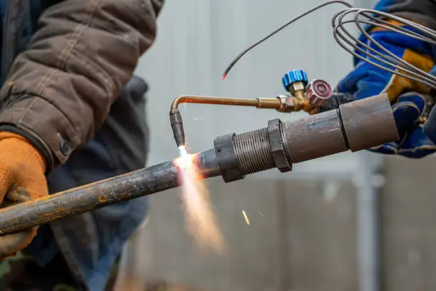 Two workers join two metal parts using an outdoor gas welder.