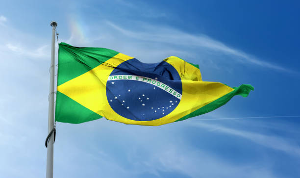 istock Brazilian flag waving on a pole in a blue sky 1461018480