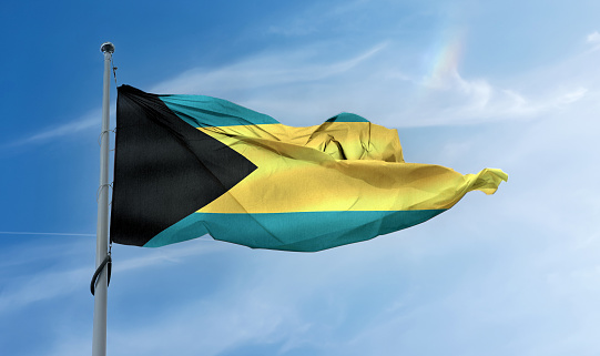 A Bahamas flag waving on a pole in a blue sky