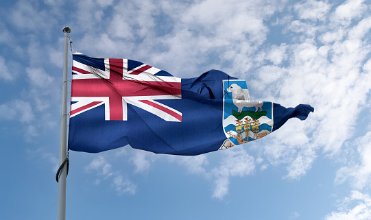 A Falkland Islands flag waving on a pole in a blue sky