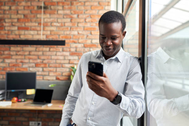 istock Smiling young businessman in small office standing with mobile phone browsing internet 1461018680