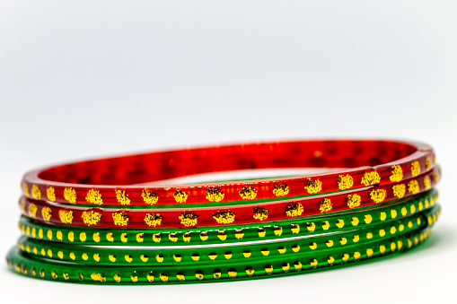 A closeup shot of red and green glass bracelets (bangles) with golden dots on a white background