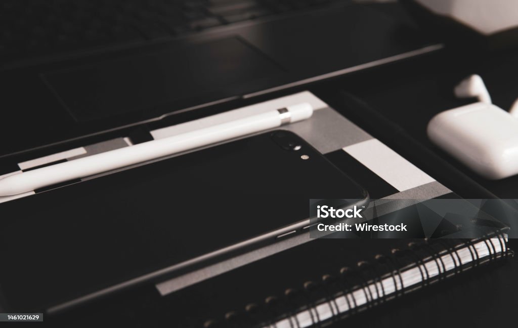 Closeup shot of a smartphone, laptop, and wireless earphones on the table in grayscale A closeup shot of a smartphone, laptop, and wireless earphones on the table in grayscale Black And White Stock Photo