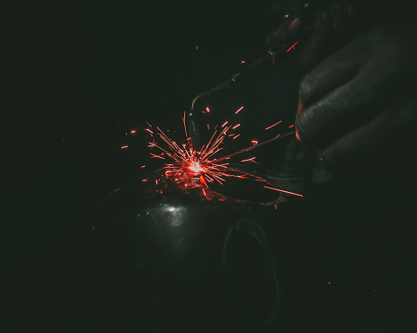 A closeup of a man welding a metal ball in the darkness