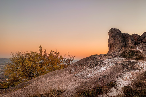 A landscape of rocks surrounded by yellowing trees during the sunset in the even