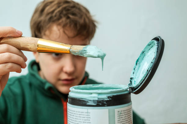 A teenager watches paint dripping from a paintbrush. Concept de new life of old things. Restoration of antique old furniture pieces. stock photo