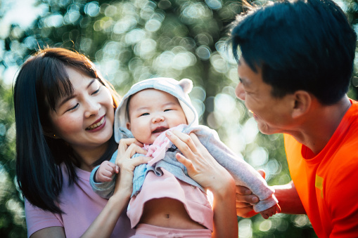 Cheerful family with cute baby girl playing outdoors on sunny day