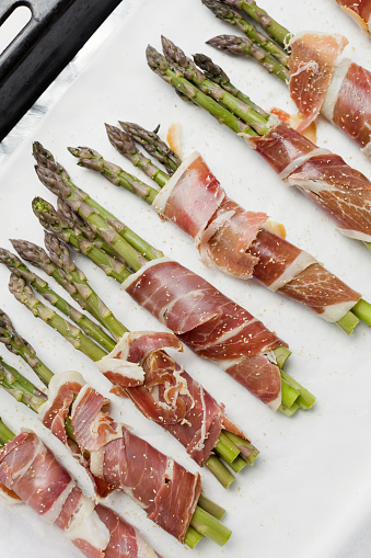Asparagus with ham on white background. Tasty spring dish with asparagus and bacon