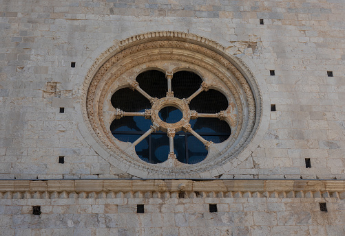 Aerial drone view of an intricate circular church window, with beautiful carving in the stone work. Set in the high structural wall of the old religious building.