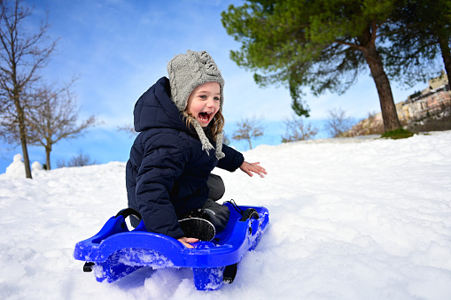 Little girl with blue sled on the hill having fun.