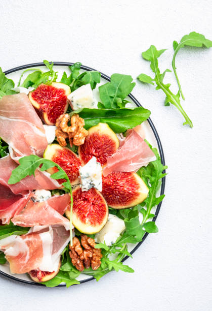 istock Fresh fig salad with prosciutto, gorgonzola, walnuts, arugula on white kitchen table background, top view, copy space 1461034966