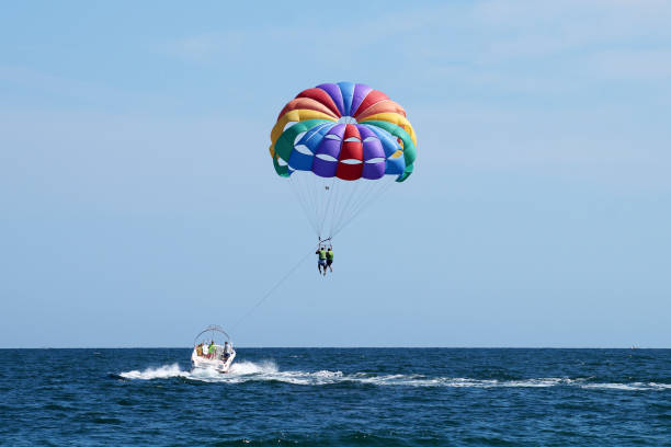 tourists flying on a multicolored parachute tied to a boat Varna, Bulgaria - September, 20, 2021: tourists fly on a multicolored parachute tied to a boat parasailing stock pictures, royalty-free photos & images