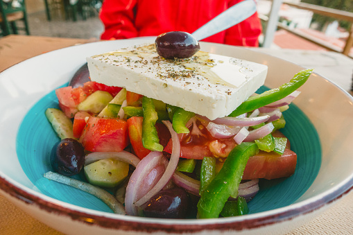 White plate with Mediterranean salad. The plate is on a rough mat. Nearby lies a napkin with a spoon and fork.