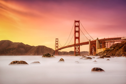 Long exposure photo in Marshall's Beach with Golden Gate Bridge in the background in San Francisco at sunset, California