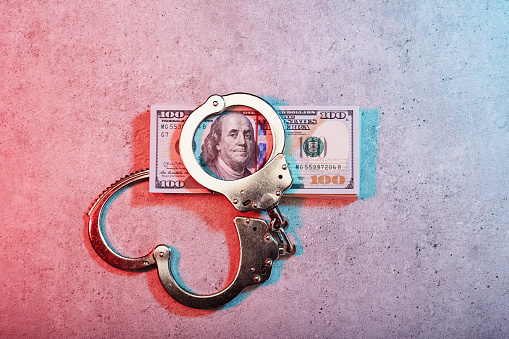 Handcuffs,stack of American one hundred dollar bills on concrete surface