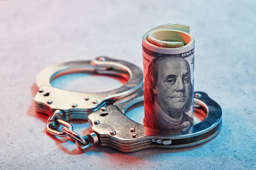 Handcuffs and roll of American one hundred dollar banknotes