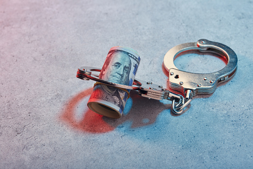 Handcuffs and roll of American one hundred dollar banknotes