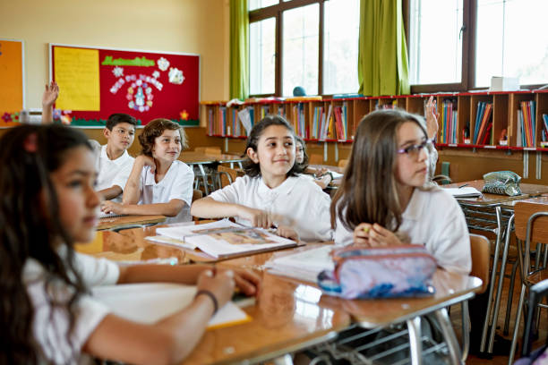 Pre-adolescent children in uniforms sitting at desks, smiling, and participating in discussion.