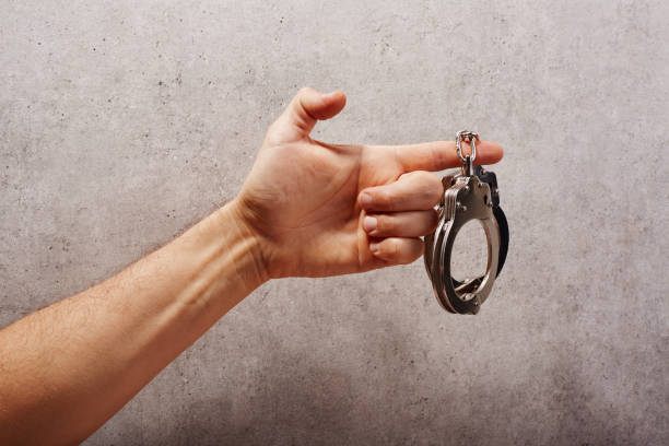 Hand holding handcuffs in front of a concrete background