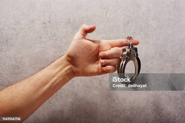 Hand Holding Handcuffs In Front Of A Concrete Background Stock Photo - Download Image Now