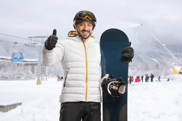 Young man with snowboard gesturing thumbs up and smiling Young man with snowboard gesturing thumbs up and smiling in a ski resort thumbs up for skiing stock pictures, royalty-free photos & images