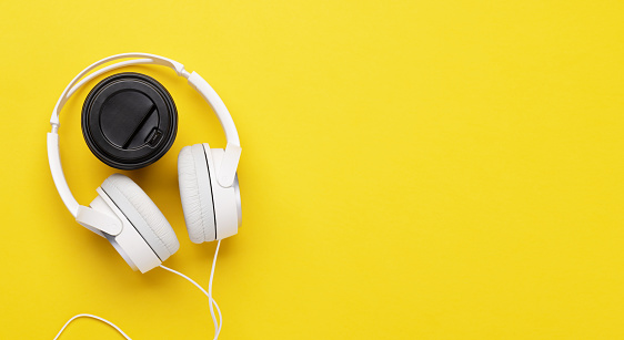 Headphones and coffee cup on yellow background. Flat lay with copy space