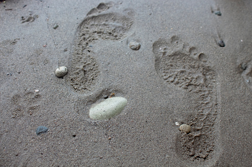 Photo of two footprints in the sand and between a small rock